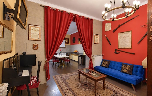A living room with a blue sofa, red curtains, a chandelier, and a dining area in the background.