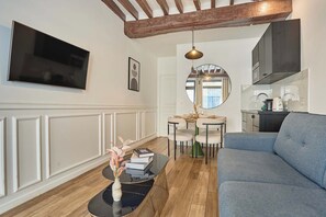A modern living room with a flat-screen TV, a sofa, a coffee table with books, and a dining area with a mirror. - Apartment in the center of Paris (Paris)