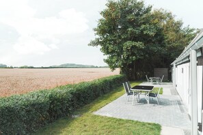 Eine Terrasse mit Tisch und Stühlen, einer Hecke und Blick auf ein Feld.