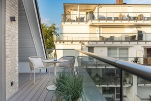 Ein Balkon mit Glastrennwand, zwei weiße Korbstühle, ein kleiner runder Tisch und eine Weinflasche.