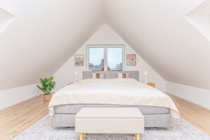Ein Schlafzimmer mit einem großen Bett, einem Nachttisch, einer Stehlampe und einem Blumentopf am Fenster.