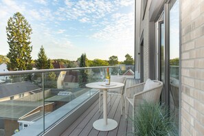 Ein Balkon mit Glasgeländer, ein runder Tisch mit Flasche und Glas sowie Korbstühle.