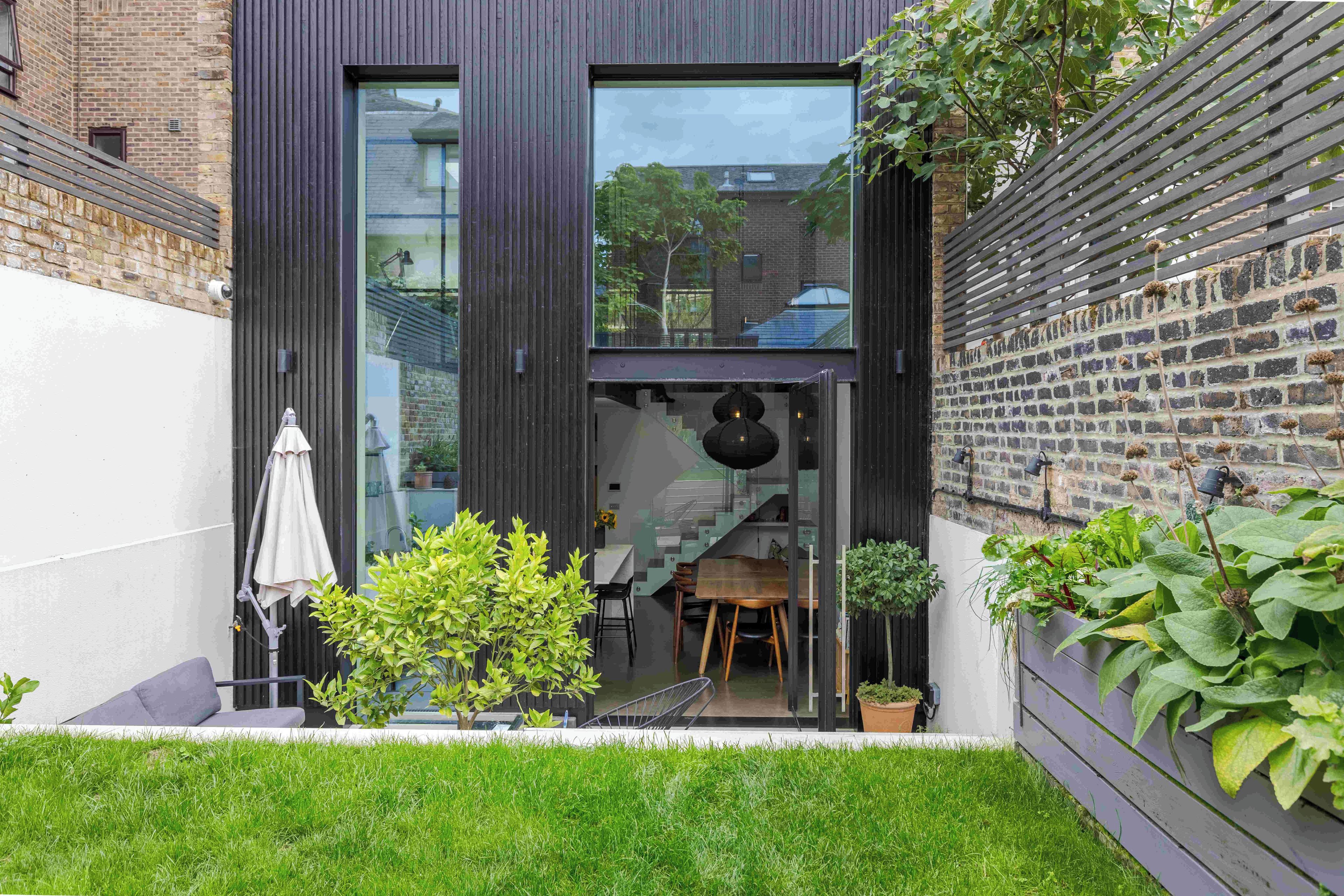 A modern building with a large glass window, a wooden deck, and a brick wall.