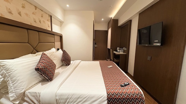 A hotel room with a large bed, a television on the wall, and a bathroom visible in the background.