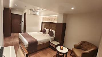 Habitación de hotel con cama, mesita de noche, silla y una pequeña mesa con frutero.