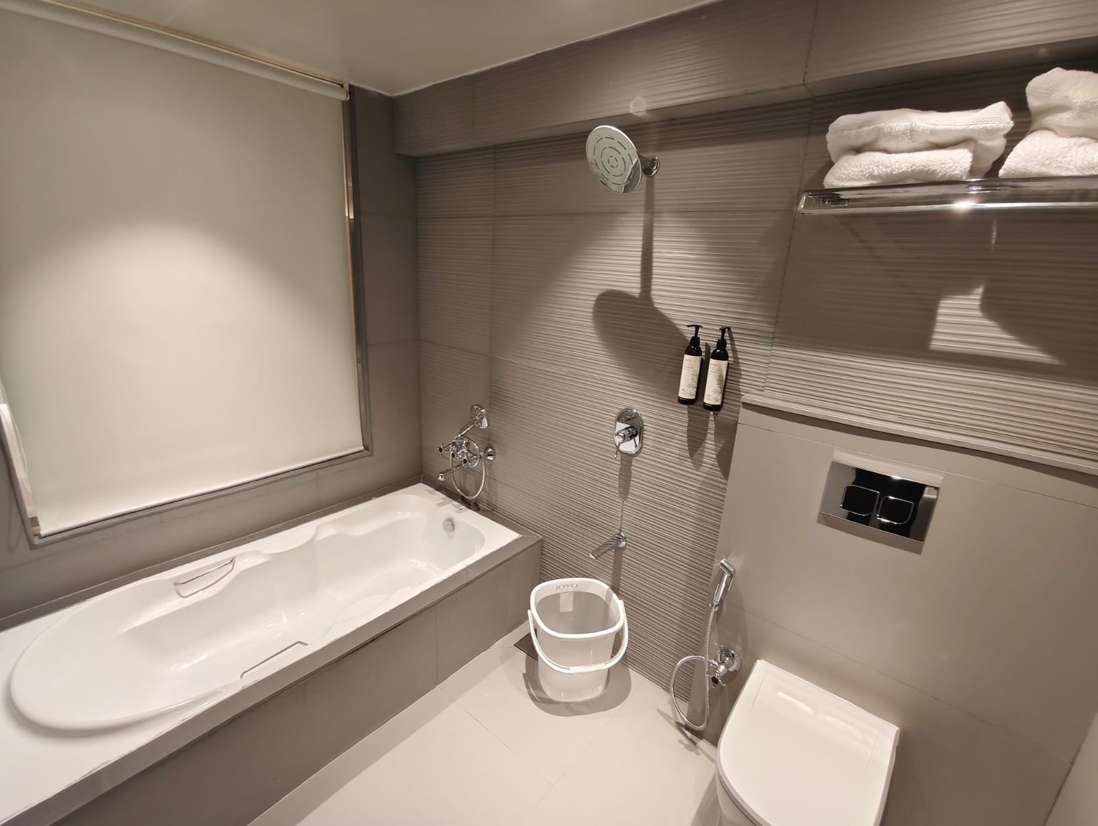 Une salle de bain moderne avec une baignoire, des toilettes et un bidet. Des serviettes sont posées sur une étagère et des articles de toilette sont accrochés au mur.