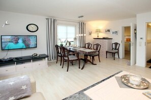 A dining area with a table and chairs, a television mounted on the wall, and a clock. - Starklef 1, Holiday Apartment 3, Rungholt (Wyk auf Föhr)