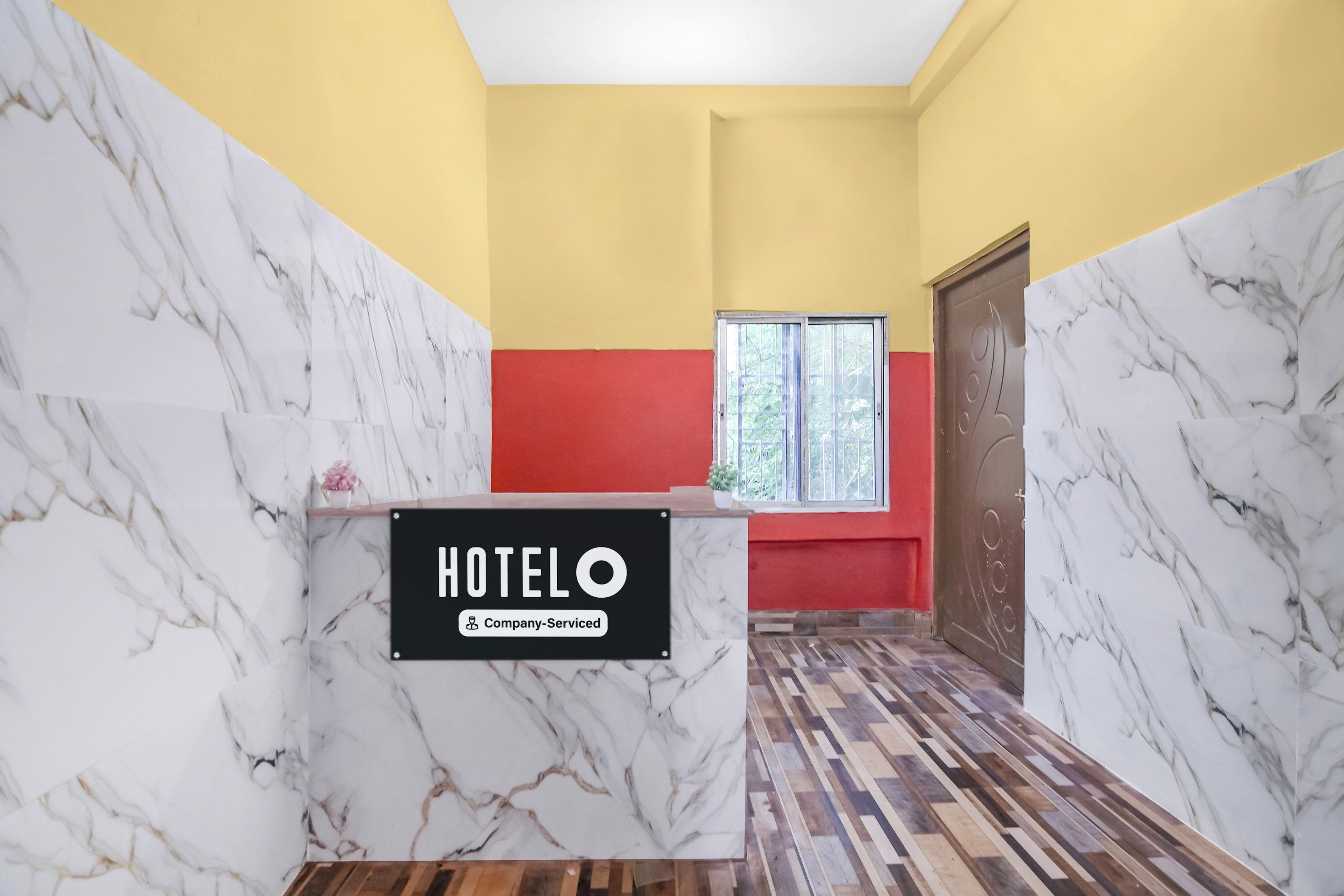 A hotel reception desk with a marble design, a red accent wall, and a window with a view.