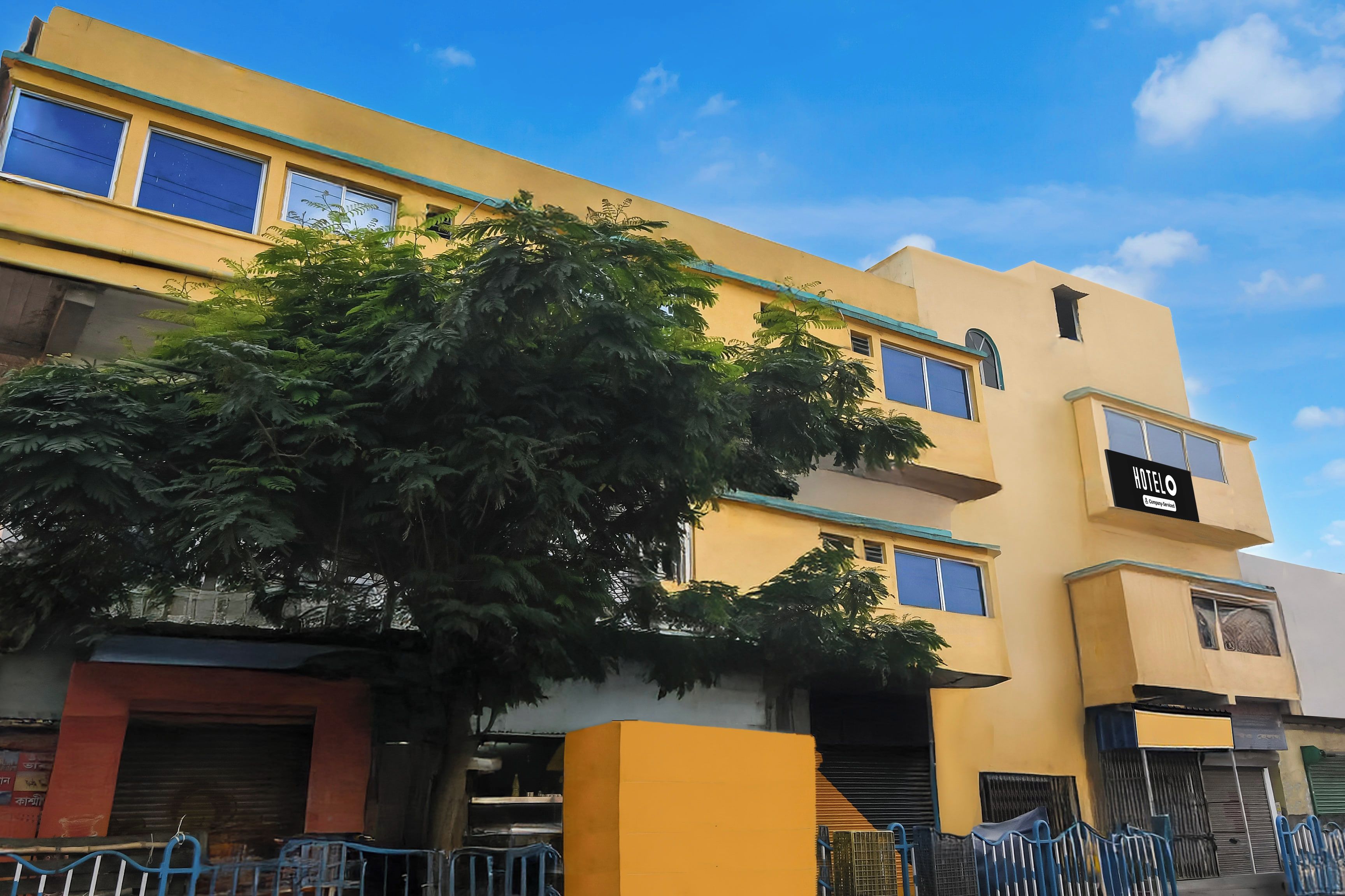 A multi-story building with a yellow facade, a tree in front, and a sign indicating a hotel.