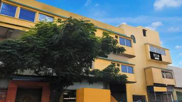 A multi-story building with a yellow facade, a tree in front, and a sign indicating a hotel.