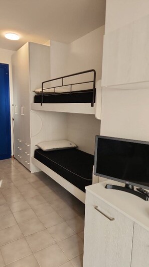 A bunk bed with a television on a cabinet, a wardrobe with drawers, and a blue door. - Renovated studio apartment just steps from the sea (Bibione)