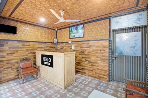 A hotel reception area with a wooden reception desk, a ceiling fan, and a patterned wall. - Hotel O Zero Bridge Formerly Time Star (Srinagar)