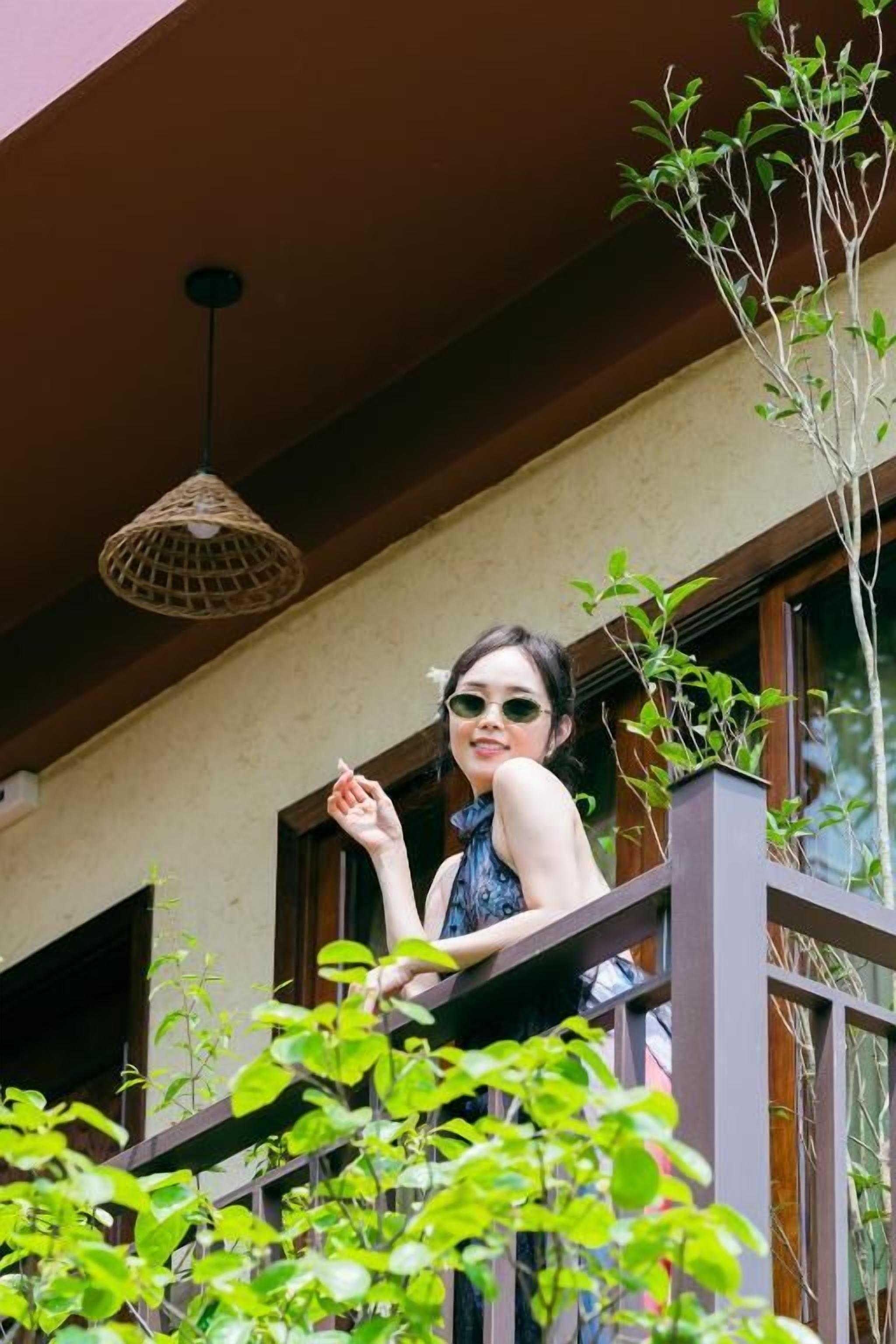 A person standing on a balcony with a view of greenery and a hanging light fixture.