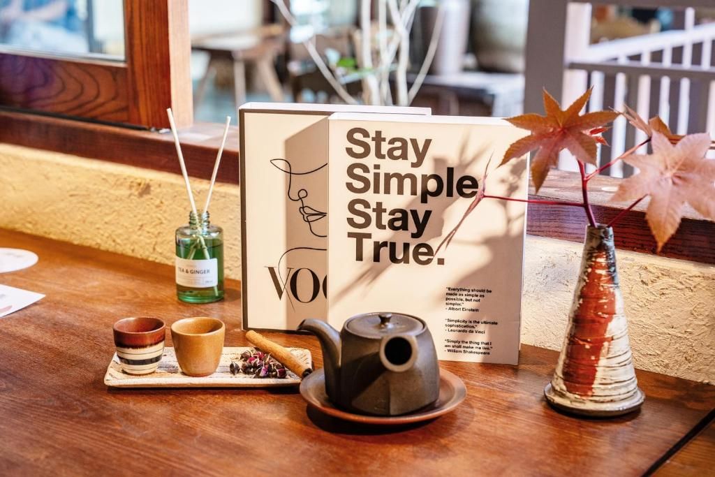 A wooden table with a tea set, a teapot, a bottle of tea & ginger, and a sign that reads 'Stay Simple Stay True.'