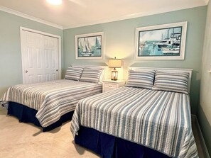 A bedroom with two beds, a nightstand with a lamp, and two framed pictures on the wall. - 8th Floor Oasis! Beautiful Gulf front views! (Panama City Beach)