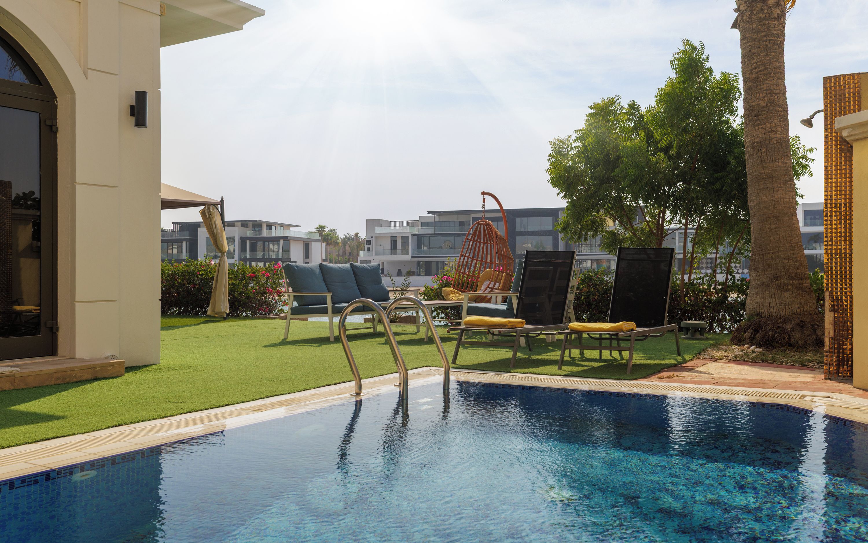 A swimming pool with lounge chairs and a hanging chair, surrounded by a well-maintained lawn and a building in the background.