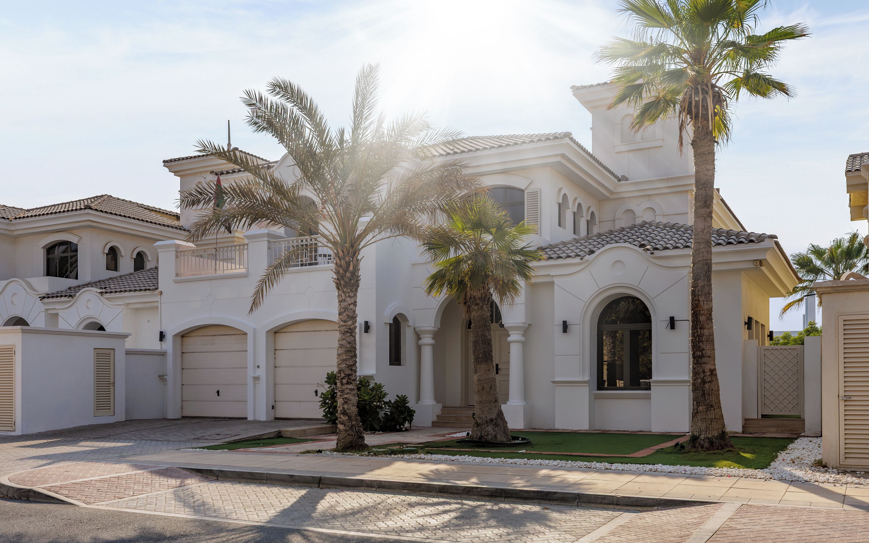 A white building with multiple garage doors, palm trees, and a paved driveway.