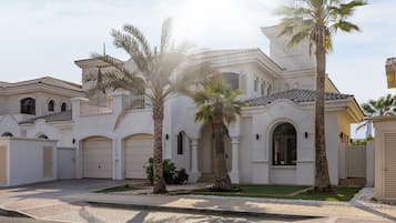 A white building with multiple garage doors, palm trees, and a paved driveway.