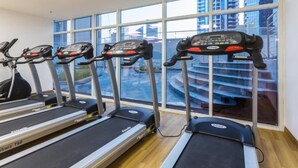Ein Fitnessraum mit Laufbändern und einem Ergometer, große Fenster mit Blick auf Gebäude.