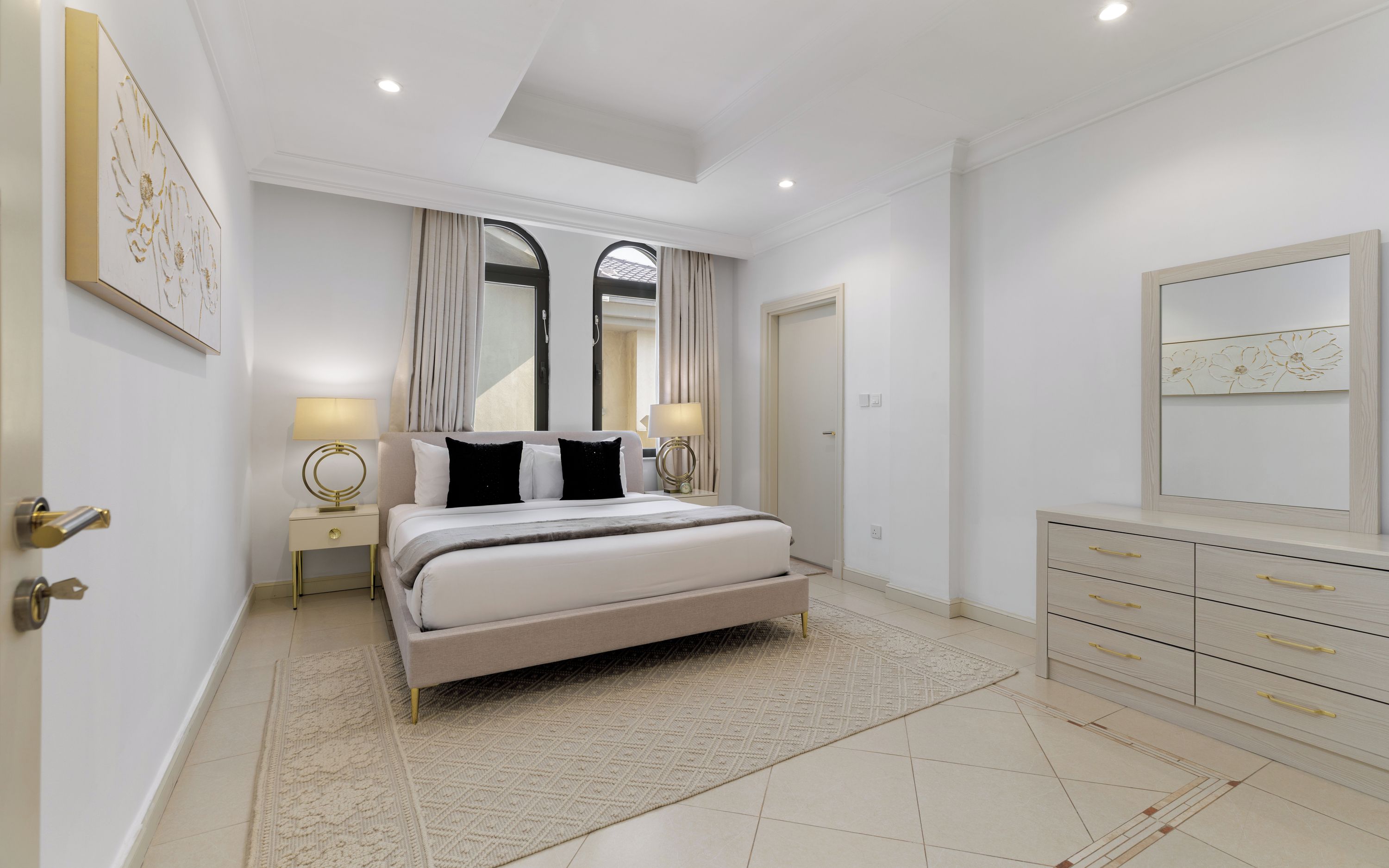 A modern bedroom with a large bed, bedside lamps, a dresser, and a mirror.