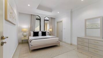 A modern bedroom with a large bed, bedside lamps, a dresser, and a mirror.