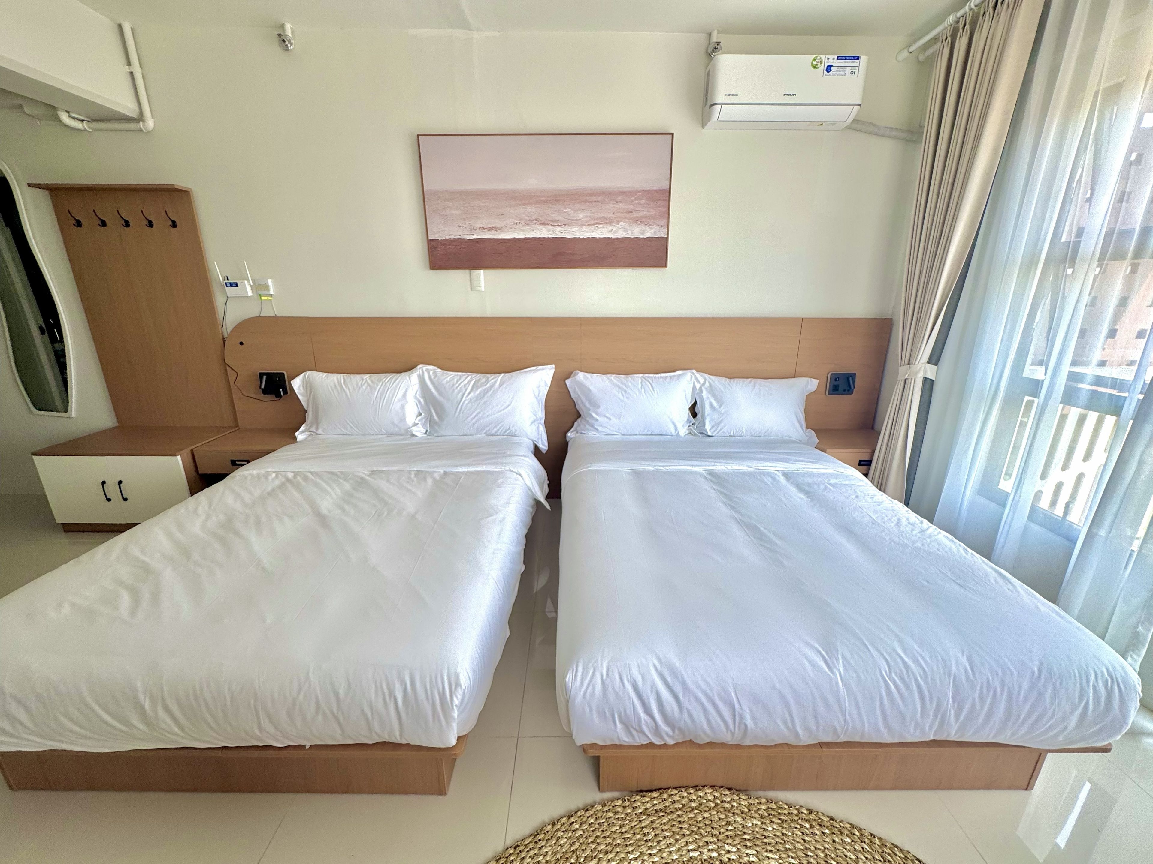 Habitación de hotel con dos camas individuales, cabecera de madera, aire acondicionado instalado en la pared y ventana con cortinas.