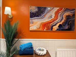 Kylpyhuone, jossa on oranssi seinä, marmorista tehty taideteos, pyyhe, koristeellinen kulho ja ruukussa oleva kasvi.