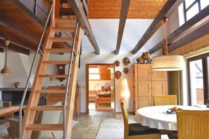 A room with a wooden staircase, a dining area with a round table, and a view of a bedroom with a bed and a window. - Devil's tail||Lenzkirch (Lenzkirch)