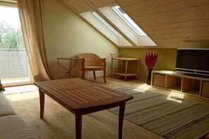 A room with a sloped ceiling, a wooden table, two wicker chairs, a television, and a large window. - Holiday apartment with 2 bedrooms (Murnau)