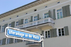 Ein Straßenschild mit dem Text 'Uferanlage an der Wacht' vor einem Gebäude mit mehreren Fenstern und Balkonen.
