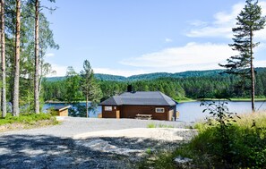 Eine Holzhütte mit Kiesweg, umgeben von Wald und einem See.