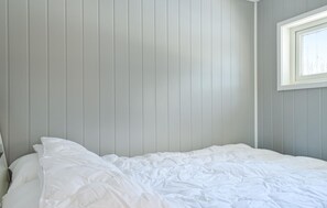 Ein Schlafzimmer mit einem Bett, weißer Bettwäsche und einem Fenster mit Jalousien.