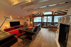 En rummelig stue med pejs, fjernsyn og stort vindue med udsigt til en balkon.