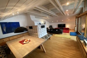 A modern living room with a wooden floor, a dining table with a red placemat, a black sofa, and a television. - Alpenflair holiday apartment 402 (Oberstdorf)