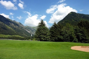 A golf course with a flag, trees, and mountains in the background. - Alpenflair holiday apartment 402 (Oberstdorf)