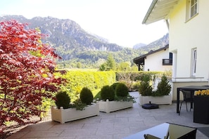 A patio area with a table and chairs, surrounded by white planters with greenery, and a view of a mountainous landscape in the background. - Holiday apartment with 1 bedroom (Schwangau)