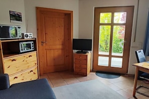 Habitación compacta con puerta de madera, televisor sobre un mueble pequeño, microondas y una mesa de comedor con una silla.