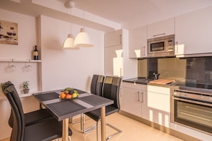 A modern kitchen with a dining table, chairs, a fruit bowl, a microwave, and a stove. - in the Riesch guesthouse | holiday apartment (Garmisch-Partenkirchen)