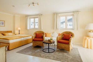 A hotel room with a bed, two wicker chairs, a small round table, and a window with curtains. - in the Riesch guesthouse | holiday apartment (Garmisch-Partenkirchen)