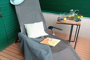 A lounge chair with a cushion, a book, and a tray with glasses and flowers. - Forest green Finnish hut Hohe Klinge (Brotterode-Trusetal)