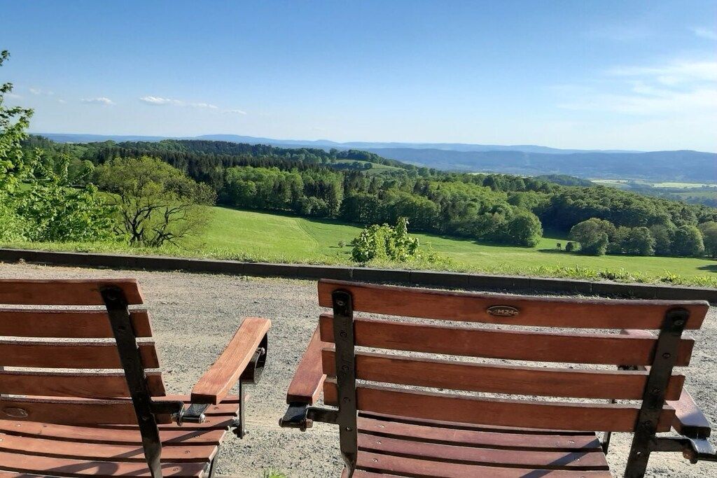 Two wooden park benches facing a scenic view of a green landscape with trees and hills.