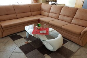 A tan leather sofa, a glass coffee table with a bottle and glasses, and a patterned rug. - Holiday apartment with 2 bedrooms (Tambach-Dietharz)