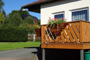 A residential building with a wooden balcony, a window, and a green lawn. - Holiday apartment with 2 bedrooms (Tambach-Dietharz)