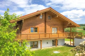 Eine Holzhütte mit Balkon, großen Fenstern und weißer Fassade.