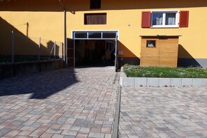 A paved entrance to a building with a yellow facade, a wooden door, and a small garden area. - Holiday apartment with 3 bedrooms (Eichstetten)