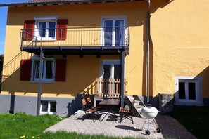 En toetagers bygning med balkon, udendørs siddepladser og grill.
