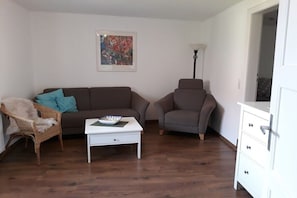A living room with a brown sofa, a white coffee table, a wicker chair, and a lamp. - Holiday apartment with 3 bedrooms (Eichstetten)