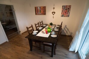 A dining area with a wooden table set for four, surrounded by chairs. There are wall decorations, a window with curtains, and a door leading to another room. - Holiday apartment with 3 bedrooms (Eichstetten)