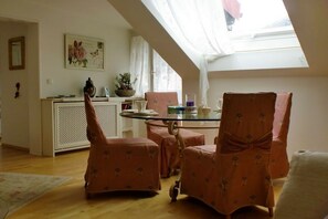 Ein Essbereich mit einem Tisch aus Glasplatte, rosa gepolsterten Stühlen und einer weißen Kommode im Hintergrund.