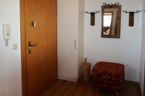 A room with a wooden door, a small wooden stool, a mirror with antler decorations, and a patterned ottoman. - Alpenflair holiday apartment 317 (Oberstdorf)